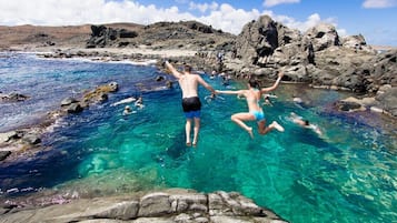 Una zona costera rocosa con aguas azules cristalinas, gente nadando y saltando al mar.