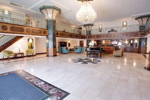 A spacious lobby with a grand chandelier, a piano, and a staircase connecting multiple levels.