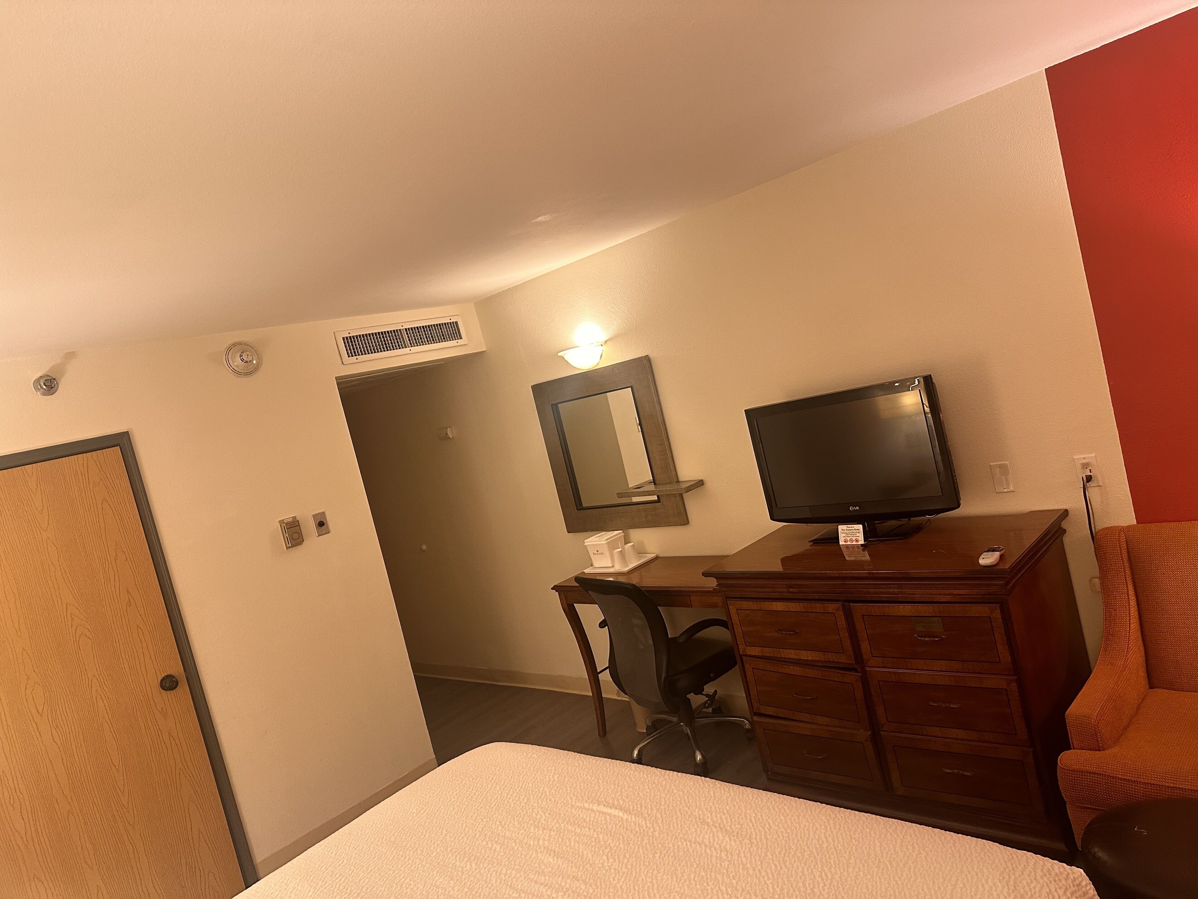 A hotel room with a bed, a desk with a computer, a TV, a mirror, and a dresser.