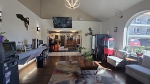 A hotel lobby with a reception desk, a coffee machine, a vending machine, a seating area with a sofa and armchairs, and a large window offering a view of the street. - Ramada by Wyndham Anchorage (Anchorage)