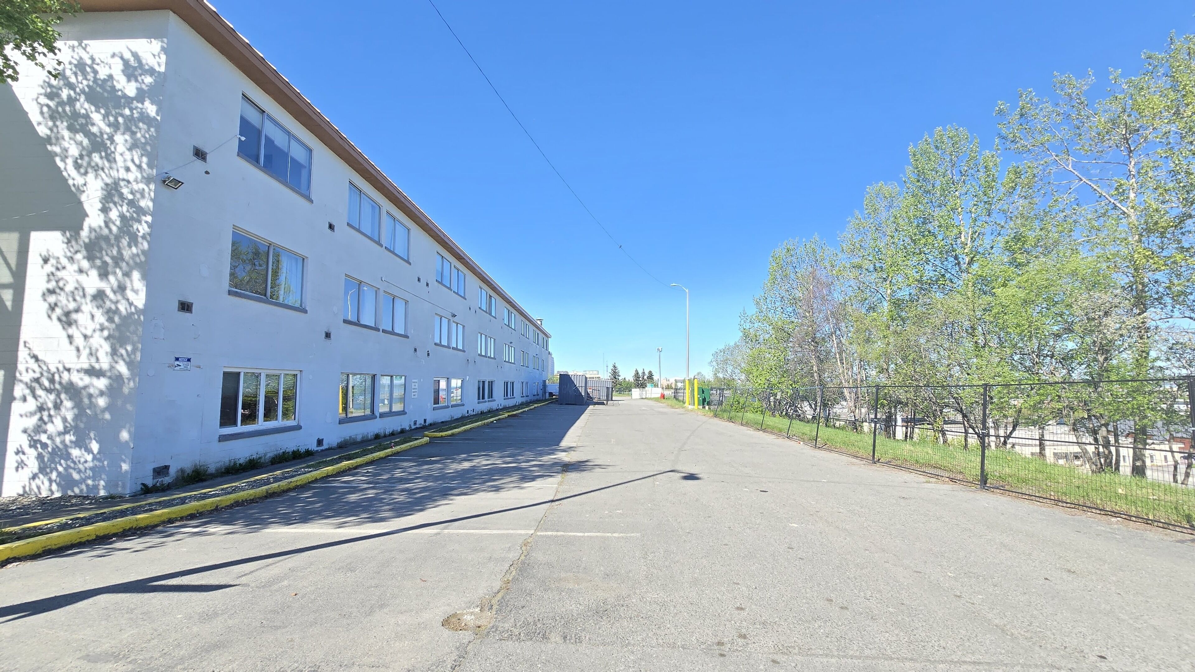 A long, straight road with a white building on the left and trees on the right.
