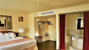 A hotel room with a bed, a desk, a chair, a shower area, and a bathroom with a bathtub. - Ramada by Wyndham Anchorage (Anchorage)