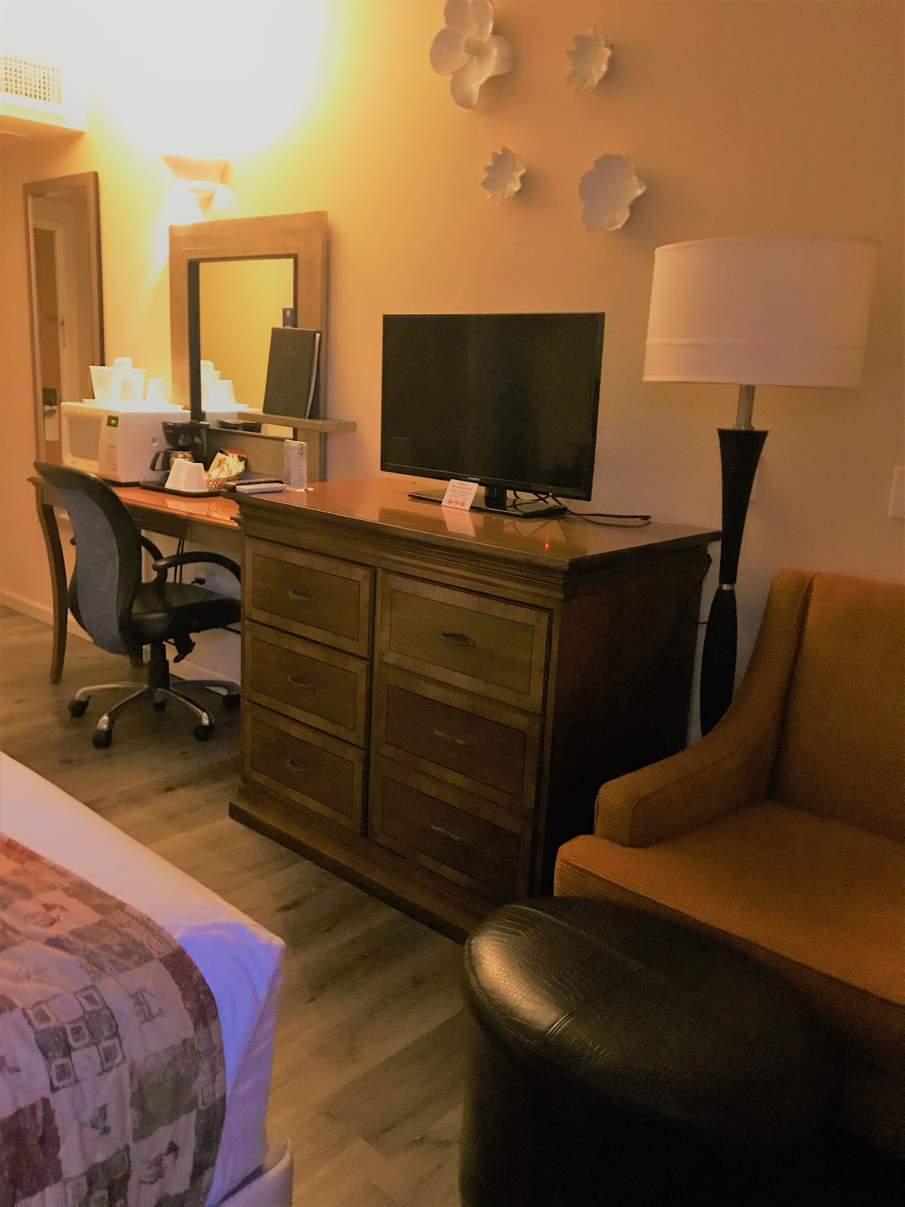 A hotel room with a desk, a television, a lamp, a chair, and a bed.