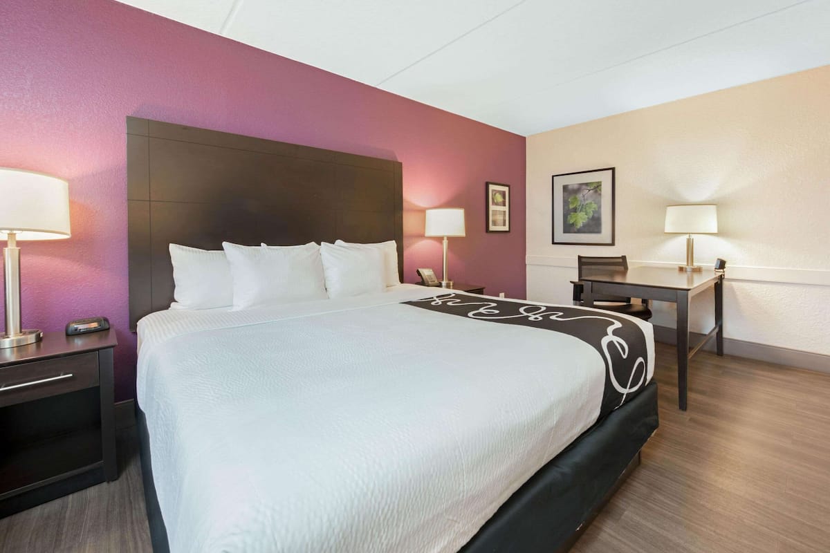 A hotel room with a large bed, two bedside tables with lamps, a desk, and a chair.