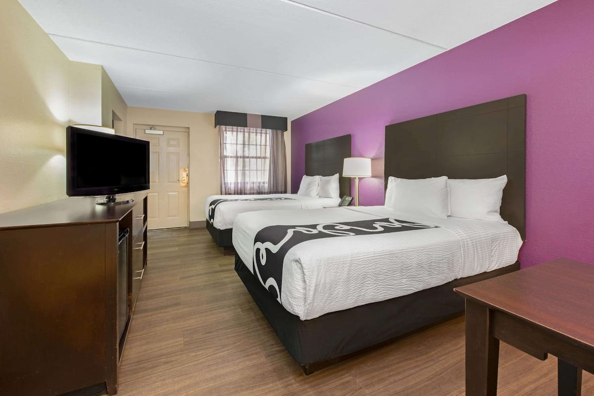 A hotel room with two beds, a TV, a desk, and a window with curtains.