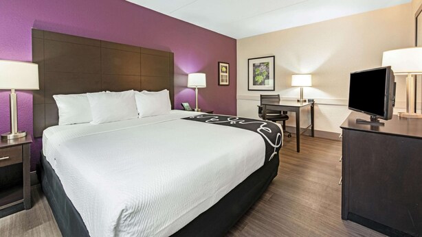 Ein Hotelzimmer mit einem großen Bett, Nachttischen, einem Schreibtisch, einem Sessel und einem Fernseher.