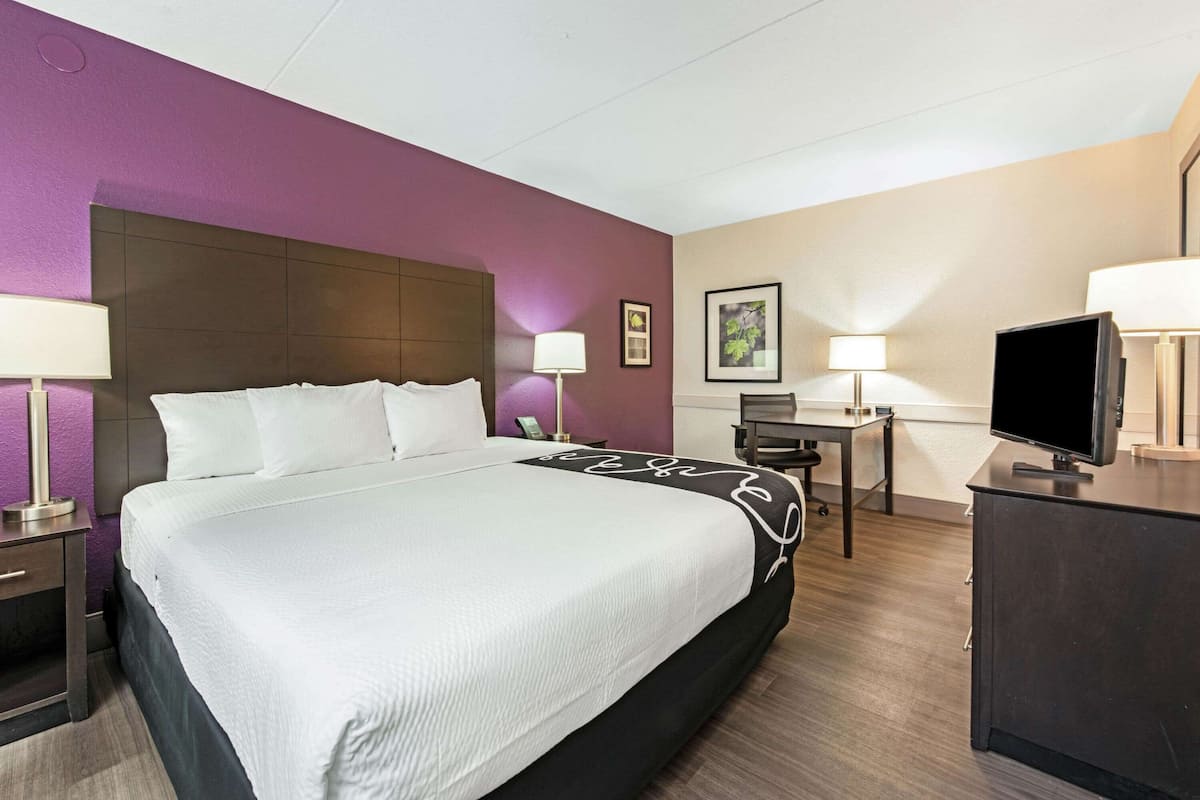 A hotel room with a large bed, bedside tables, a desk, a chair, and a television.