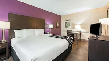 A hotel room with a large bed, bedside tables, a desk, a chair, and a television.