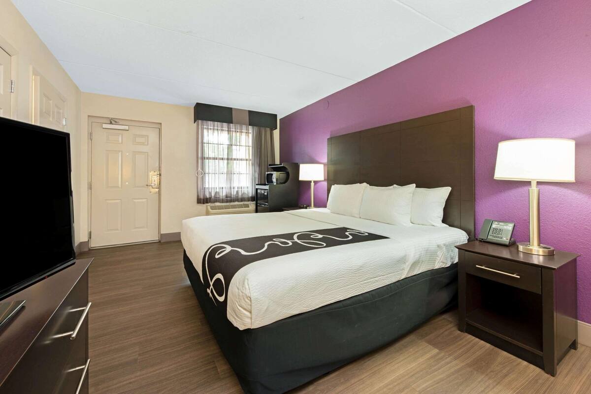 Une chambre d’hôtel avec un lit, des lampes de chevet, une télévision et un bureau avec une lampe.