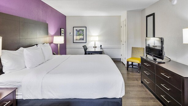 Ein Hotelzimmer mit einem großen Bett, einem Schreibtisch mit Stuhl, einem Fernseher und einem Schminktisch.