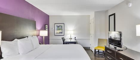A hotel room with a large bed, a desk with a chair, a television, and a dresser.