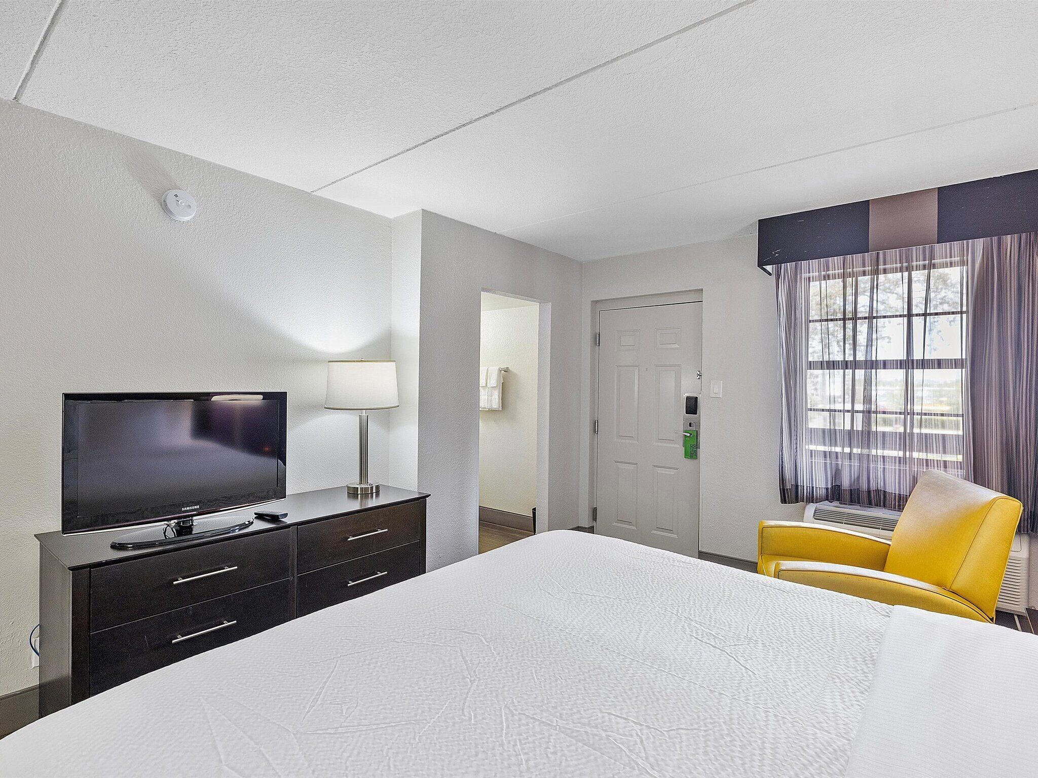 Une chambre d’hôtel avec un lit, un téléviseur posé sur une commode, une chaise et une fenêtre avec des rideaux.