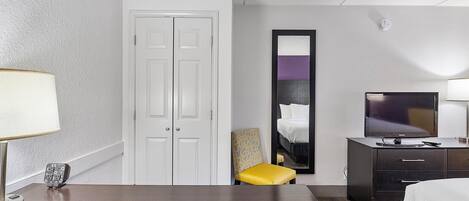 Een hotelkamer met een bed, een bureau met lamp, een televisie, een stoel en een kledingkast.