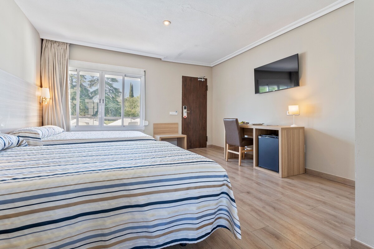 A hotel room with a large bed, a desk, a chair, and a TV mounted on the wall.
