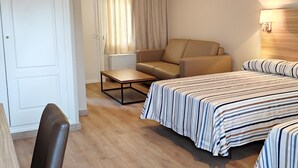 Una habitación de hotel con cama, una silla, una mesita y una ventana con cortinas.