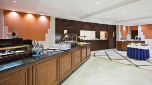 Vestíbulo de hotel con zona de bufé, mostrador de recepción y área de descanso con mantel azul.