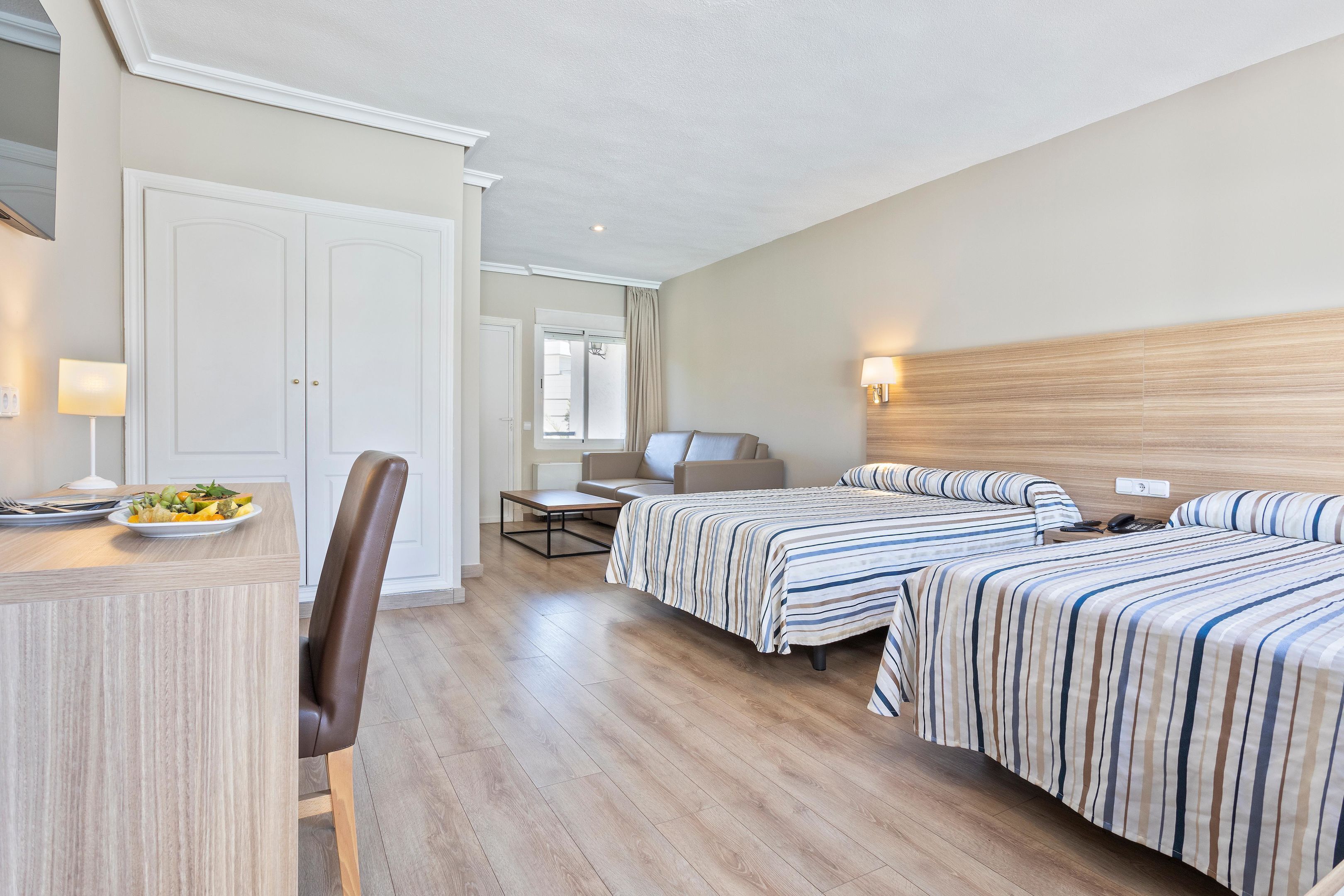 A hotel room with two beds, a desk, and a chair. There is a dining table with a plate of food.
