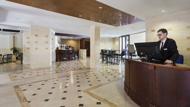 Vestíbulo de hotel con mostrador de recepción, zona de estar y suelo de baldosas.