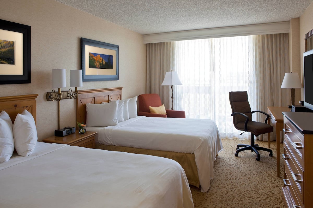 A hotel room with two beds, a desk, a chair, a TV, and a window with curtains.