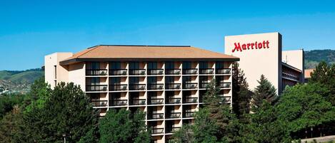 Un hotel Marriott de varios pisos con un letrero llamativo, rodeado de árboles y un cielo despejado.