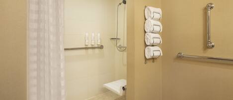 A shower area with a glass door, a handrail, and a towel rack with folded towels.