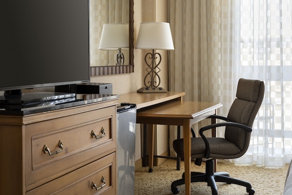 Une chambre d’hôtel équipée d’un bureau en bois, d’une chaise, d’une télévision, d’une lampe et d’un mini-bar.