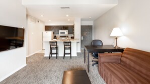 A modern living room with a flat-screen TV, a brown sofa, a coffee table, and a dining area with a table and chairs. - Value Suites Extended Stay - Arlington (Arlington)