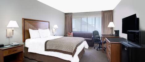 A hotel room with a large bed, a desk, a television, and a window with curtains.