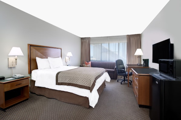 Una habitación de hotel con una cama grande, un escritorio, un televisor y un ventanal con cortinas.