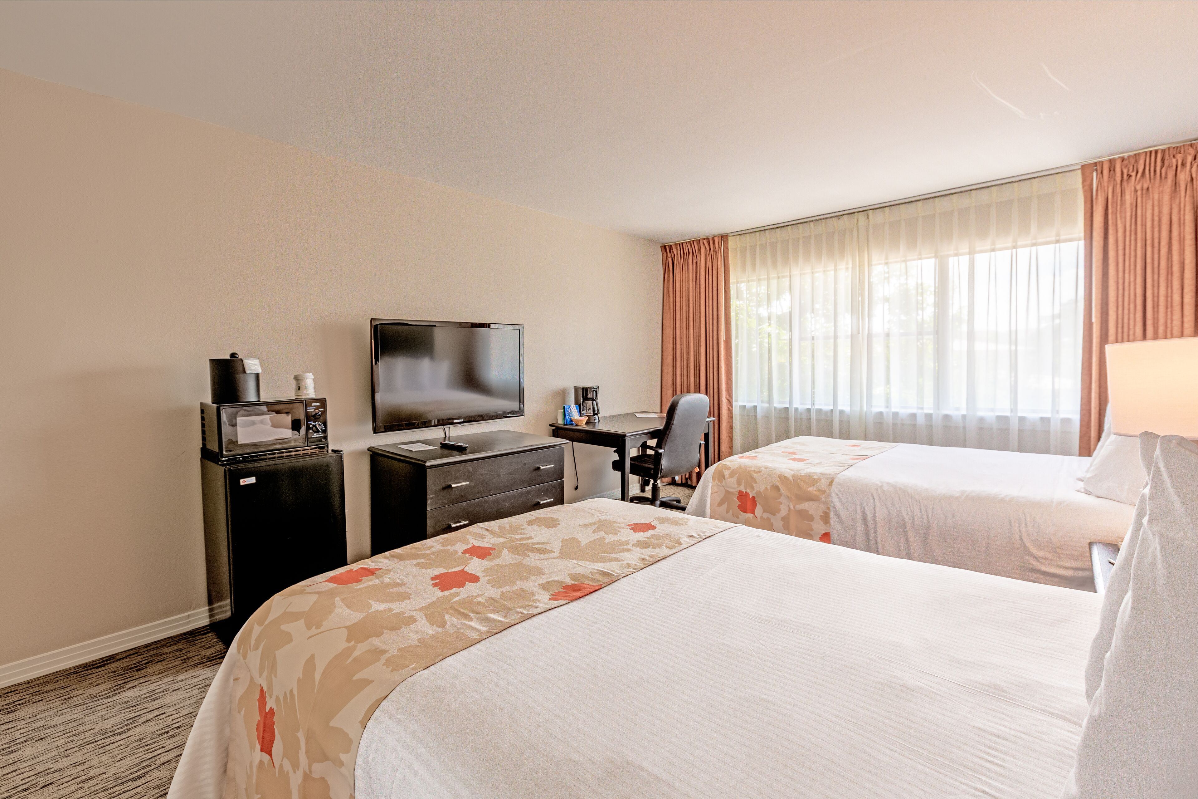 Une chambre d’hôtel avec deux lits, un bureau avec une télévision, un mini-réfrigérateur et une chaise.