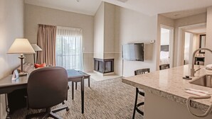 A hotel room with a desk, chair, TV, fireplace, and a kitchen area with a sink and countertop. - Value Suites Extended Stay - Arlington (Arlington)