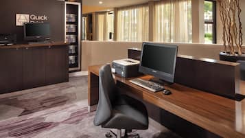 A reception desk with a computer, printer, and a chair. There is a bookshelf with books and a sign that says "Quick."