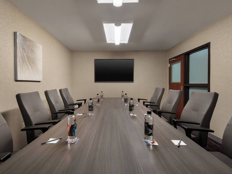 A conference room with a long table, chairs, a flat-screen TV, and a painting on the wall.