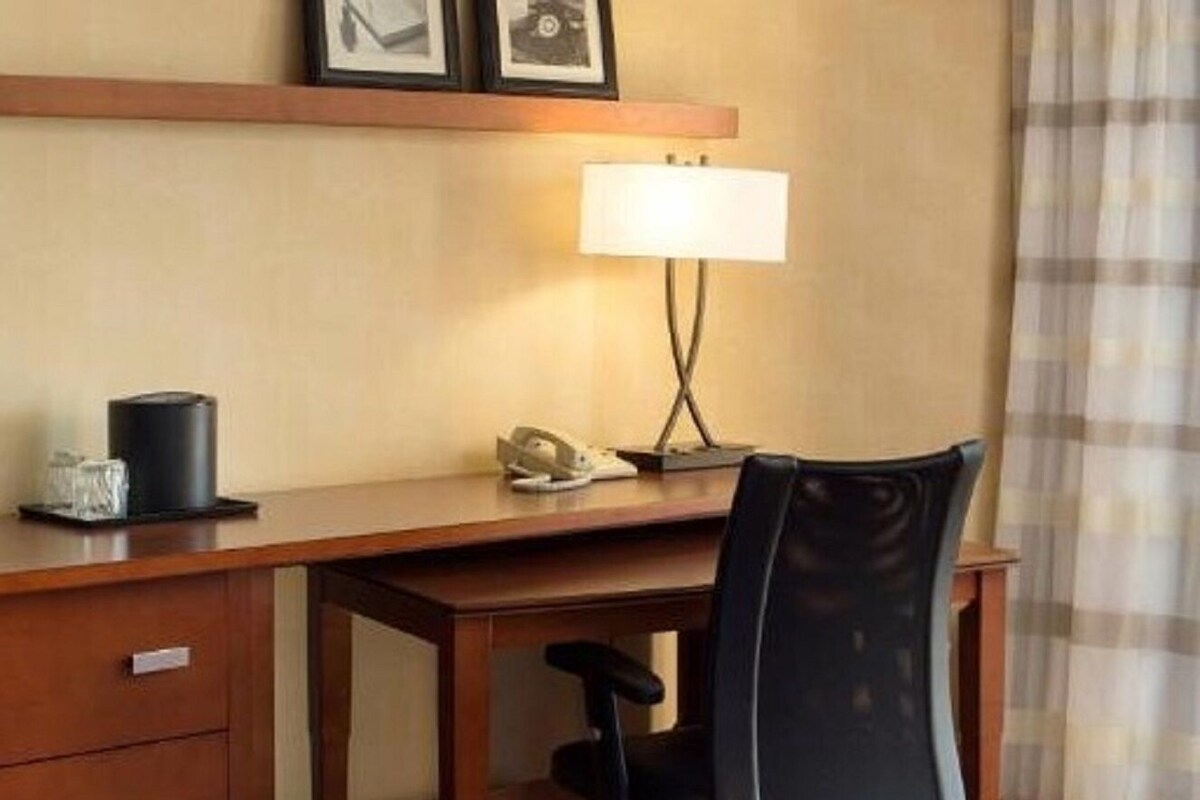 A hotel room with a wooden desk, a black office chair, a lamp, a telephone, and a coffee machine.