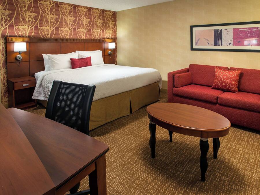Una habitación de hotel con una cama, un sofá rojo, una mesa de madera y piso alfombrado.