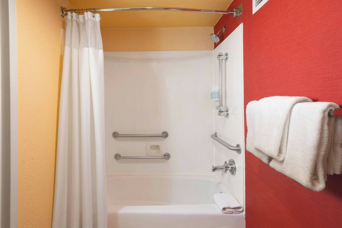 A bathroom with a shower, grab bars, a towel rack, and a red wall.