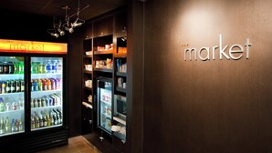 Mostrador refrigerado con diversas bebidas y aperitivos, un letrero que dice 'the market', y una pared de madera con la palabra 'market' en letras iluminadas.