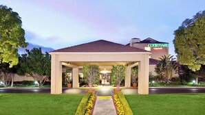 Entrada de un hotel con un corredor cubierto, un letrero de Marriott y jardines bien cuidados.