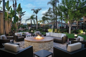 An outdoor seating area with a circular fire pit surrounded by wicker furniture and a stone fire table. - Courtyard by Marriott Costa Mesa South Coast Metro (Santa Ana)