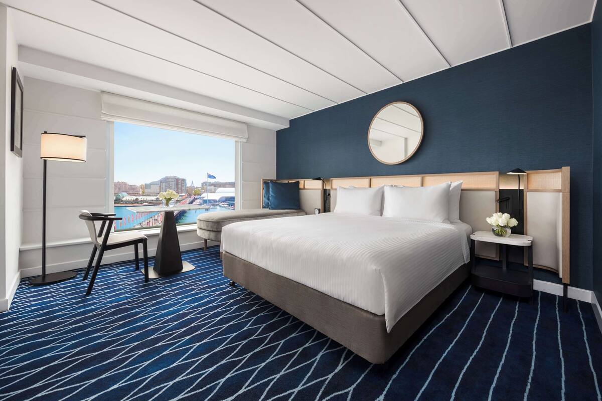 Camera d'albergo con un letto grande, uno specchio rotondo, una scrivania con una lampada e vista su un porto turistico.