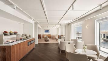 A modern hotel lobby with a wooden reception desk, seating area, and large windows offering a city view.