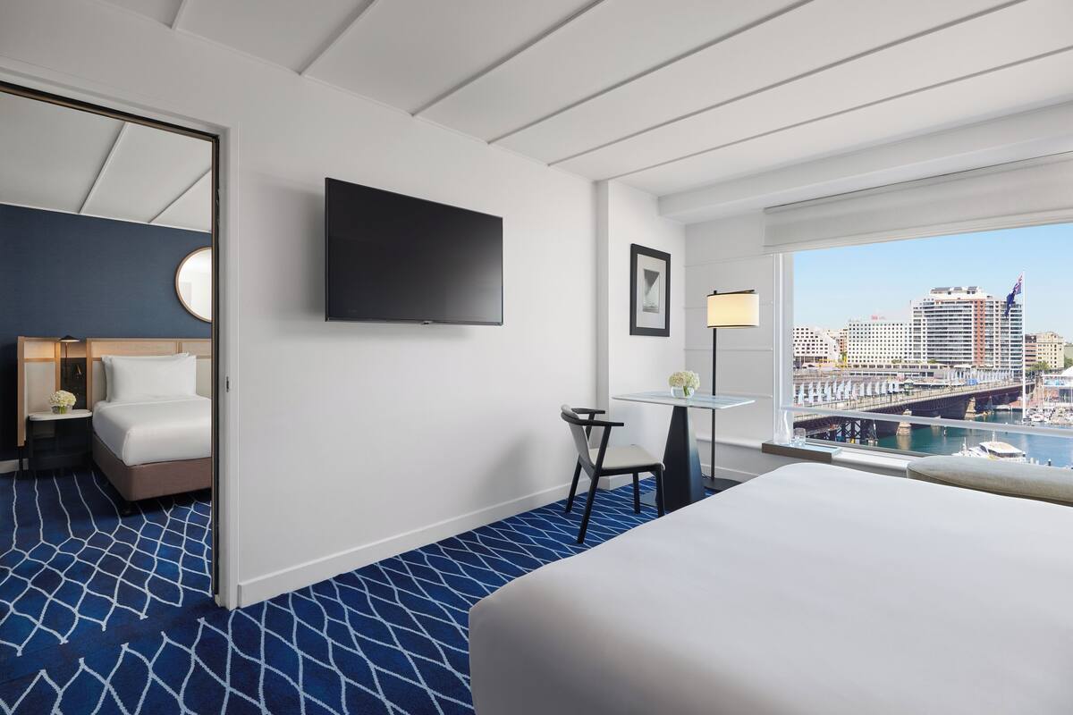 Una camera d'hotel con un letto, una scrivania, una sedia, una TV e una finestra con vista sulla città, e un tappeto a motivi.