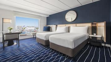 A hotel room with two beds, a desk, a chair, a round mirror, and a view of the city.