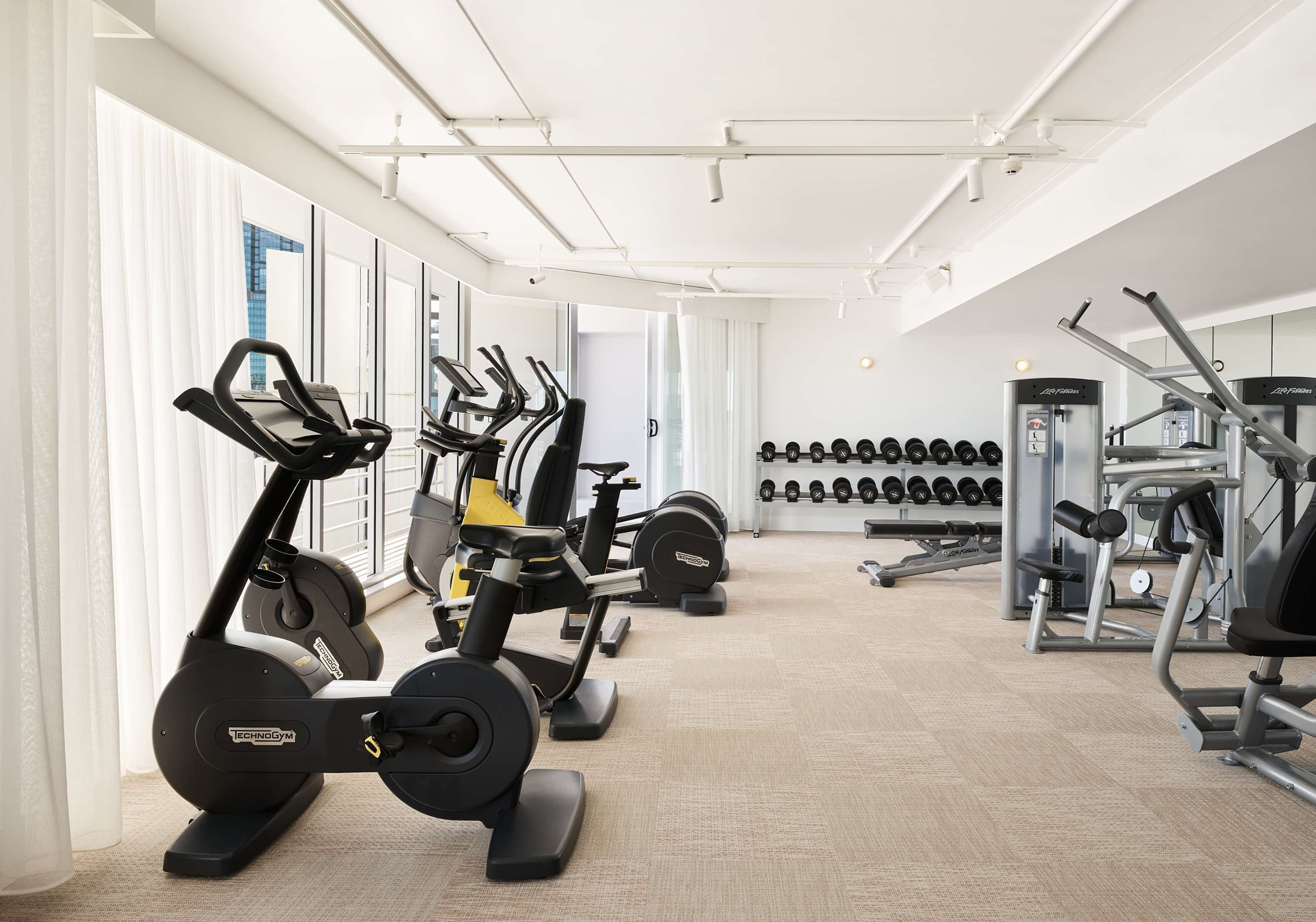 A gym with cardio machines, weightlifting equipment, and dumbbells.