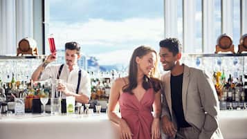 A bar area with a bartender preparing drinks, a woman in a dress, and a man in a suit.