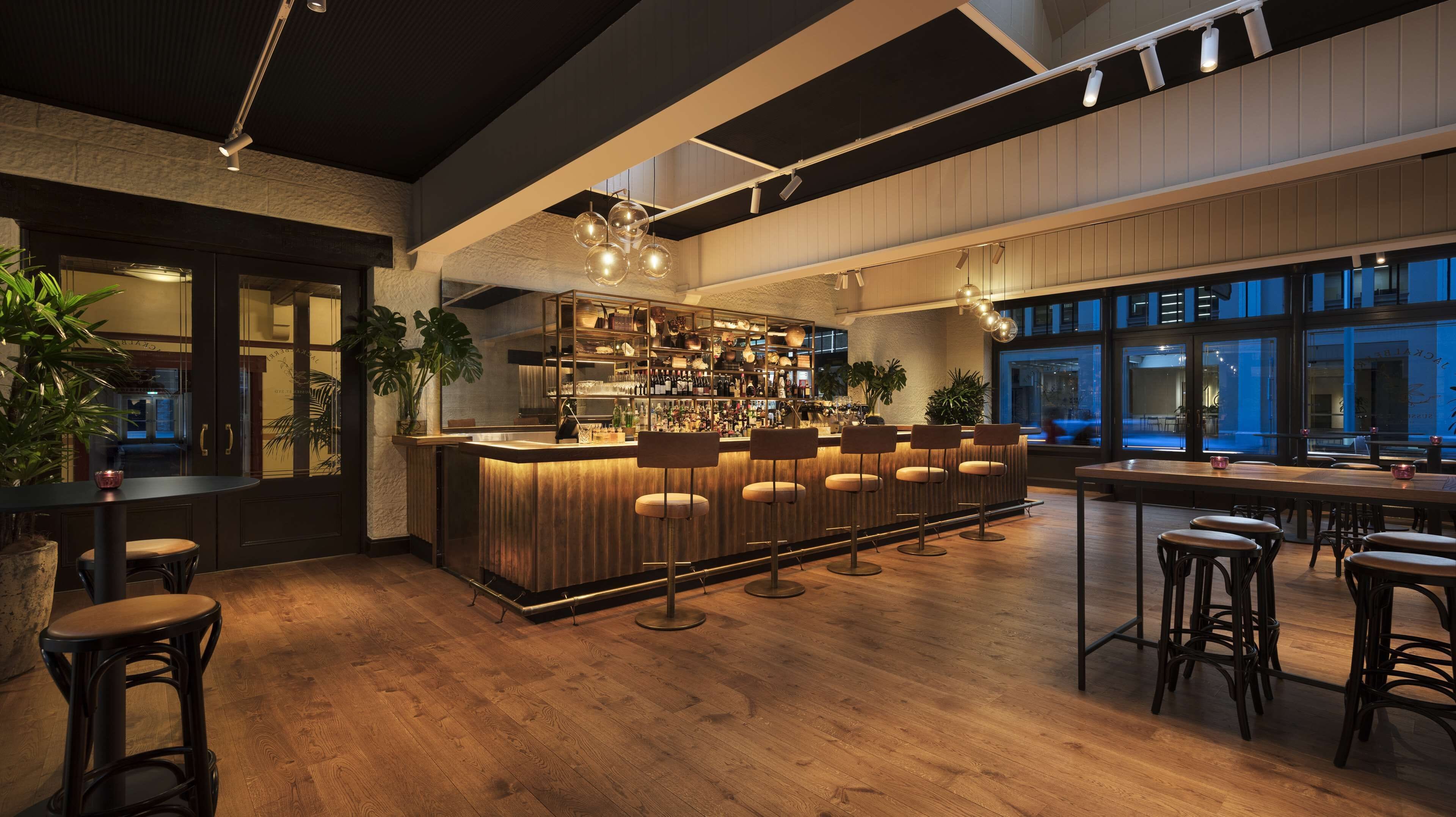 Un espace bar doté d’un plancher en bois, de tabourets de bar et d’un comptoir bien éclairé, avec des étagères remplies de bouteilles.