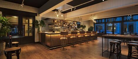 Una zona de bar con suelo de madera, taburetes y una barra bien iluminada con estantes llenos de botellas.