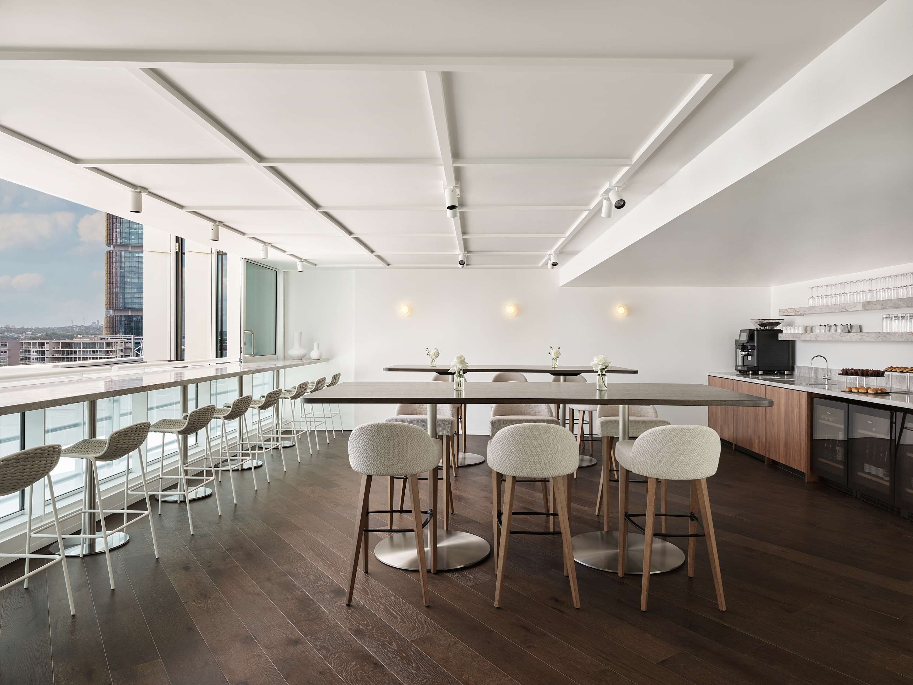 A modern kitchen with a coffee machine, a bar area with stools, and a large window overlooking a cityscape.
