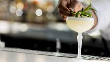 A hand adding mint leaves to a cocktail in a glass.