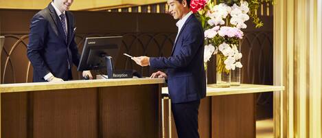 A reception desk with a Lenovo computer, a black suitcase, and a floral arrangement.